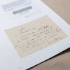 A faded, pale yellow label with many lines of handwritten old German cursive script. It sits on a piece of white card with a stamped number and barcode label above.